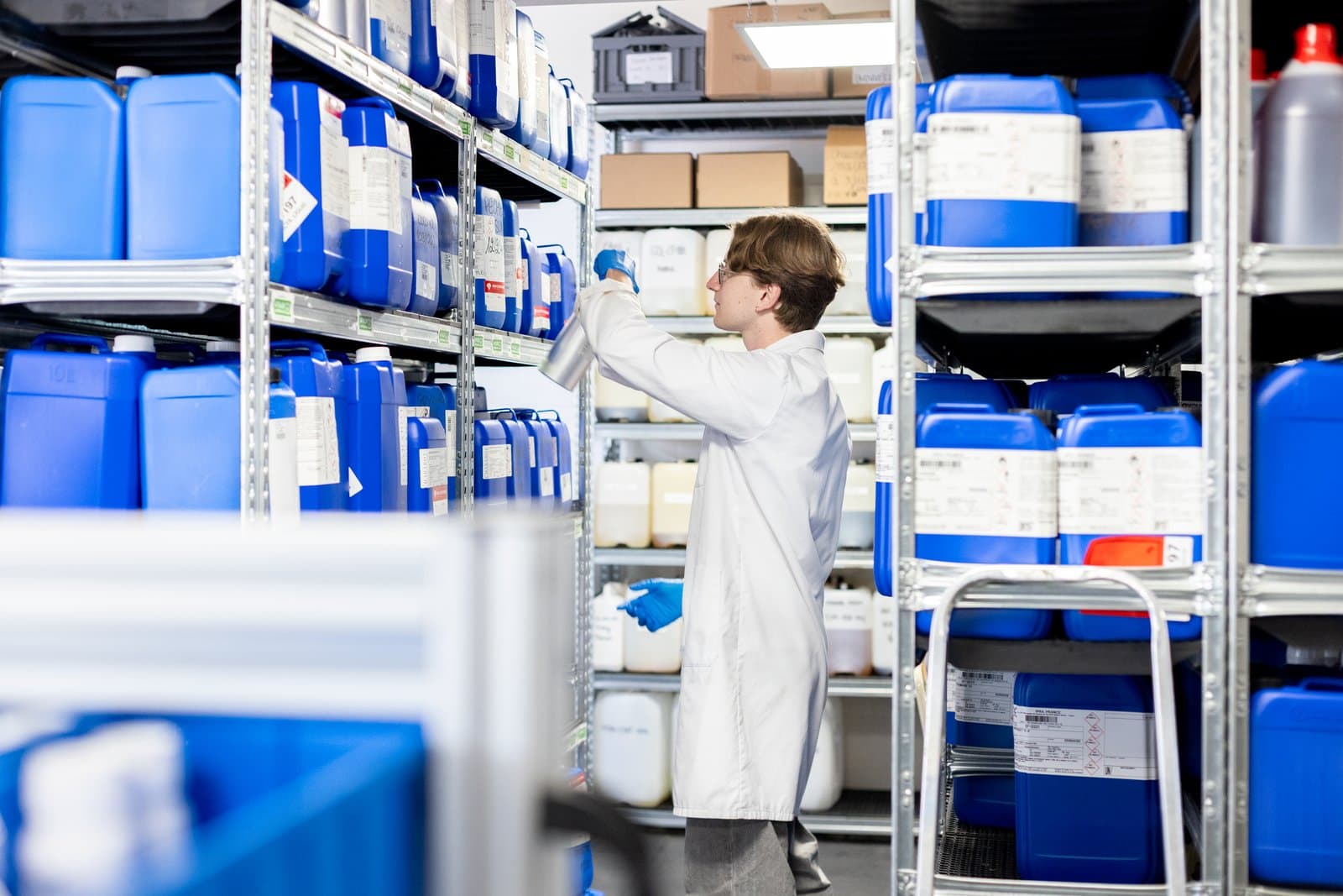 Une personne en blouse choisit un bidon sur les étagères du laboratoire.